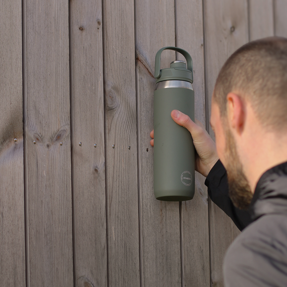Person holding a green water bottle against a wooden background