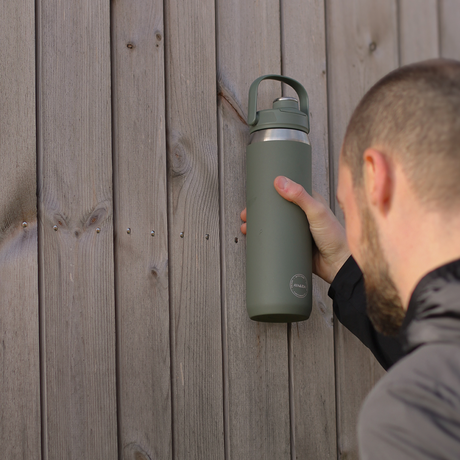 Person holding a green water bottle against a wooden background